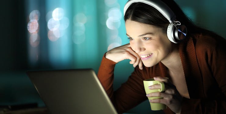 mulher sorri enquanto assiste algo no computador tomando um café