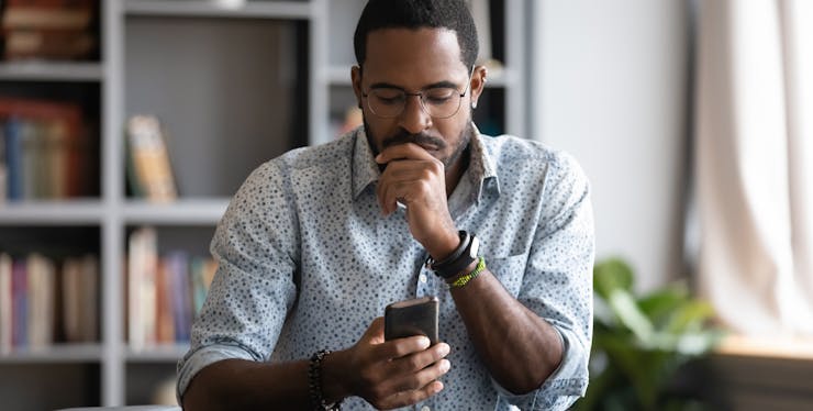 homem pensativo enquanto olha para o celular