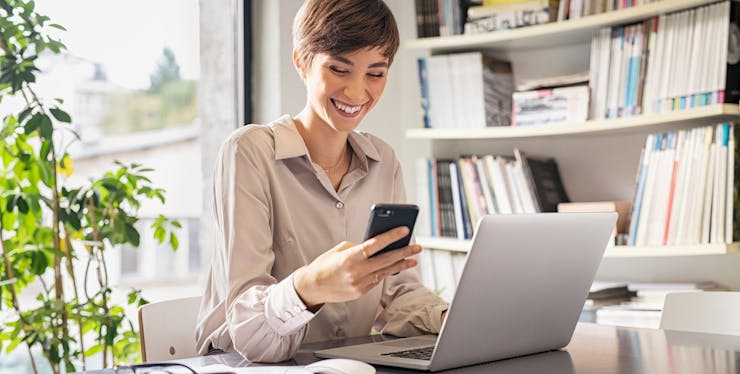 mulher sorrindo com um celular e um notebook