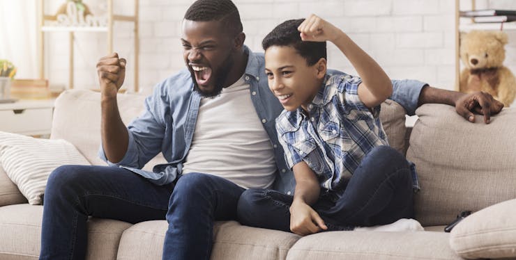 homem e criança comemorando enquanto assistem tv num sofá