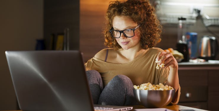 Filmes online: Jovem comendo pipoca assistindo algo no computador