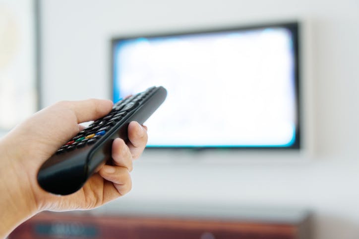 mão segurando um controle remoto em frente a uma TV
