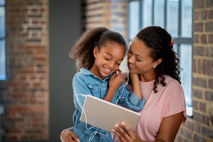 Mulher e criança assistem juntas a algum programa pelo tablet, enquanto compartilham o fone de ouvido