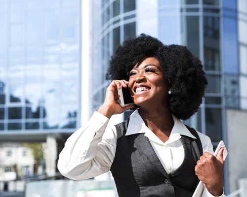 Mulher sorridente em área empresarial com celular.