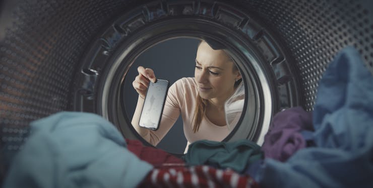 mulher tirando o celular molhado da máquina de lavar