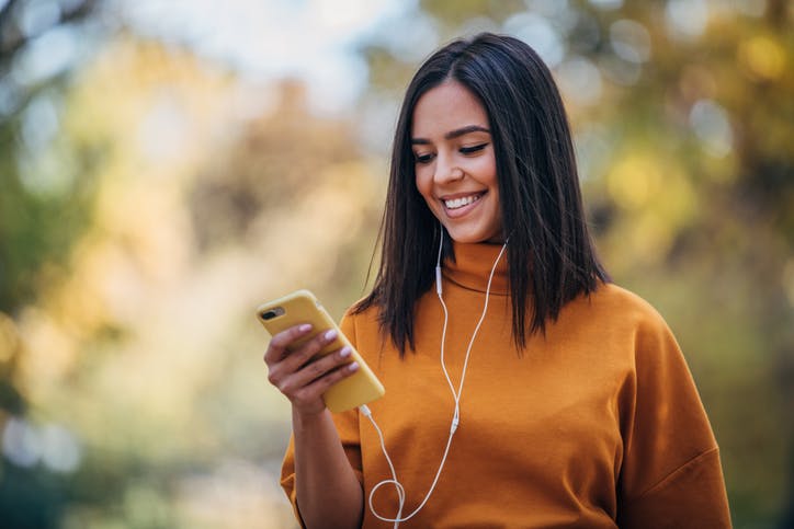 Mulher na rua escutando música em seu fone e mexendo no celular