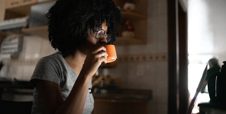 Mulher negra com uma caneca na mão olhando o computador