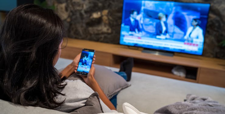 mulher espelha imagem do celular na tv enquanto assiste um telejornal
