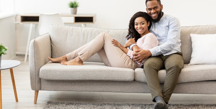 casal sorri enquanto se abraçam sentados no sofá