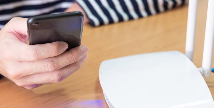 pessoa segurando celular ao lado de um roteador
