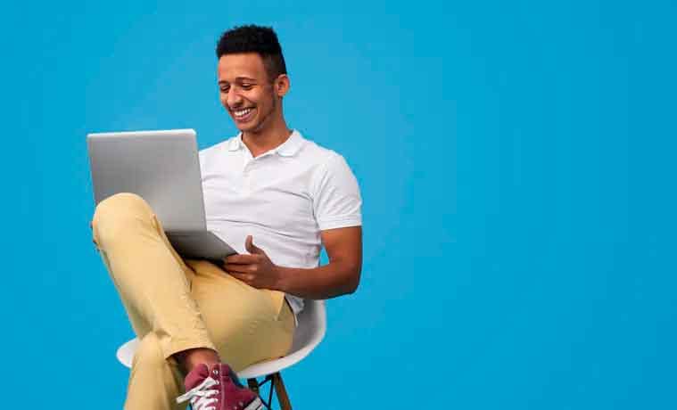 Homem sorrindo sentado com notebook no colo usando a internet NET