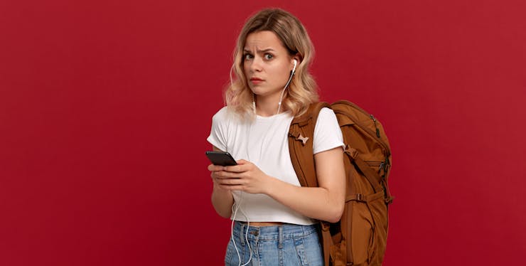 Moça com celular na mão e expressão de dúvida.