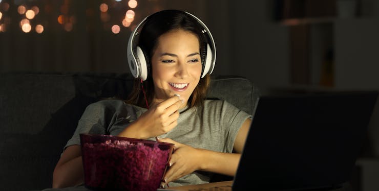 mulher sorri enquanto come pipoca e assiste streaming