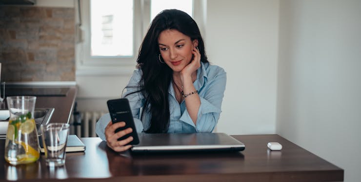mulher sentada em mesa de escritório com celular na mão