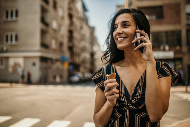 Mulher na rua tomando sorvete e falando ao celular