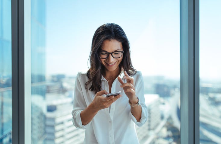 mulher sorridente olhando para o celular em sua mão