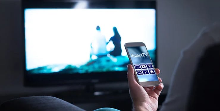Pessoa com aplicativo da smart tv aberta em frente à televisão