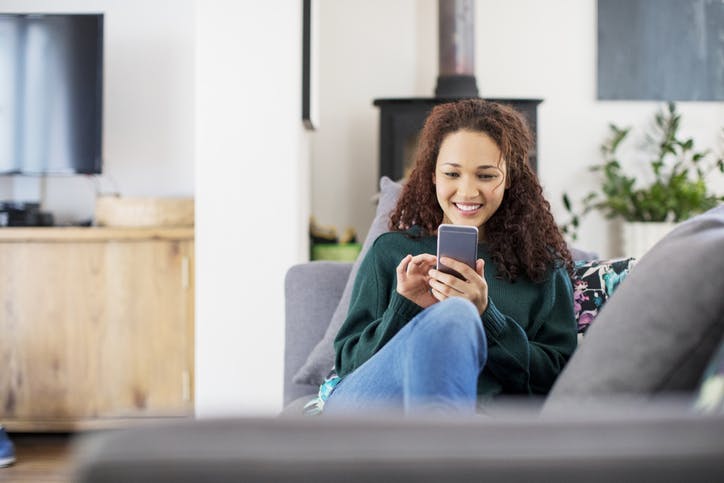 Mulher deitada e sorrindo mexendo no celular