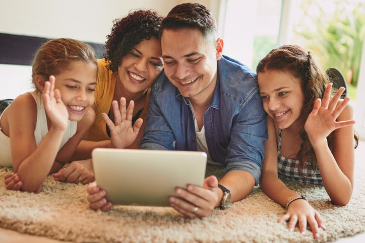 Família deitada no chão da sala falando em uma vídeo-chamada no tablet