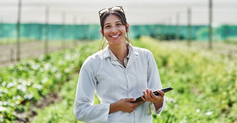 mulher em uma plantação, sorrindo e segurando um tablet