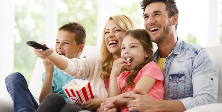 familia dando risada enquanto assistem tv e comem pipoca