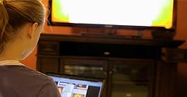 Mulher usando notebook enquanto assiste TV