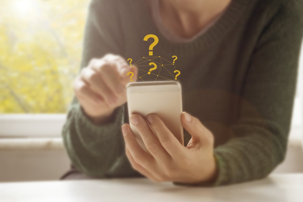Pessoa olhando celular com sinais de interrogação em volta