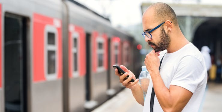 homem mexe no celular na plataforma do trem