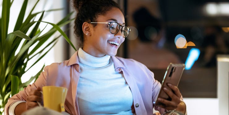 mulher sorrindo sentada no sofá com celular na mão