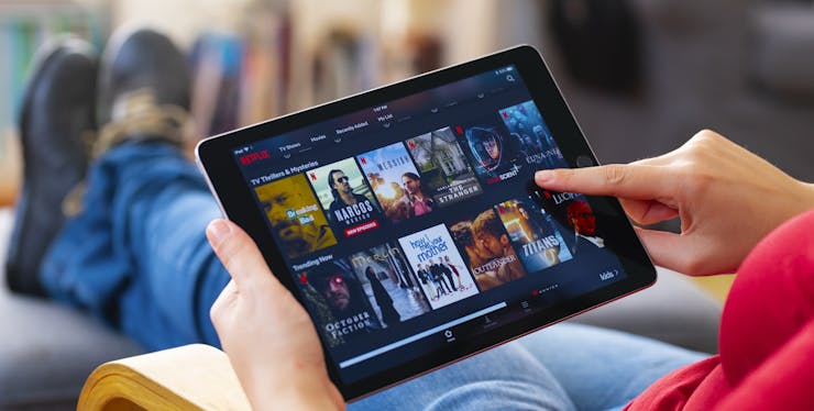 Pessoa sentada mexendo no tablet vendo Netflix