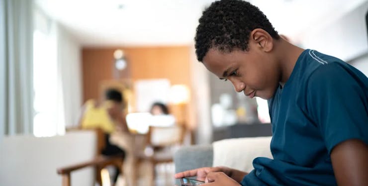 menino negro sentado em um sofá olhando o celular