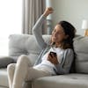 mulher feliz e comemorando sentada no sofá e com celular na mão