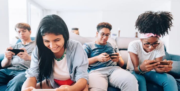 4 adolescentes sentados em um sofá branco olhando o celular