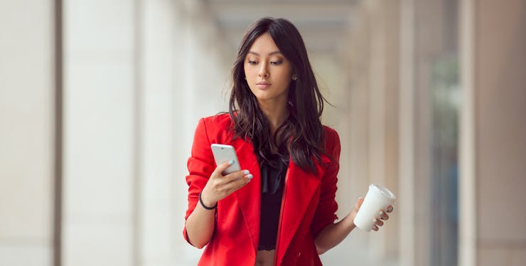 Mulher olhando o celular em um corredor com um copo na mão