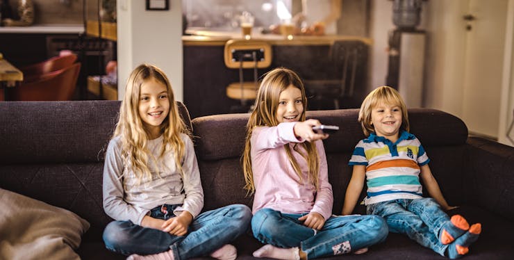 três crianças sentadas no sofá assistindo televisão
