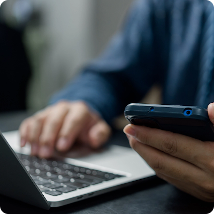 Homem segurando celular em frente ao notebbok