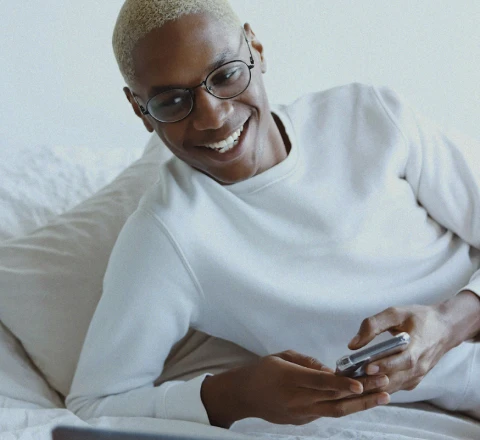 Homem deitado no sofá sorrindo com seu smartphone na mão