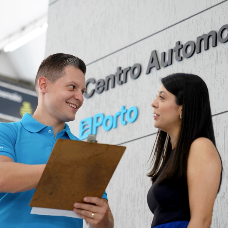 Em um Centro Automotivo Porto Serviço, um técnico segurando uma prancheta sorri e conversa com uma cliente.