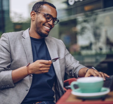 Imagem de homem sorrindo em um café com o seu cartão PortoBank em mãos