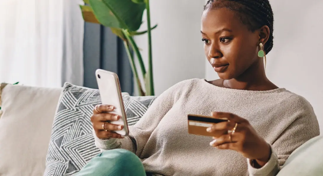 Mulher com um celular e um cartão de crédito nas mãos