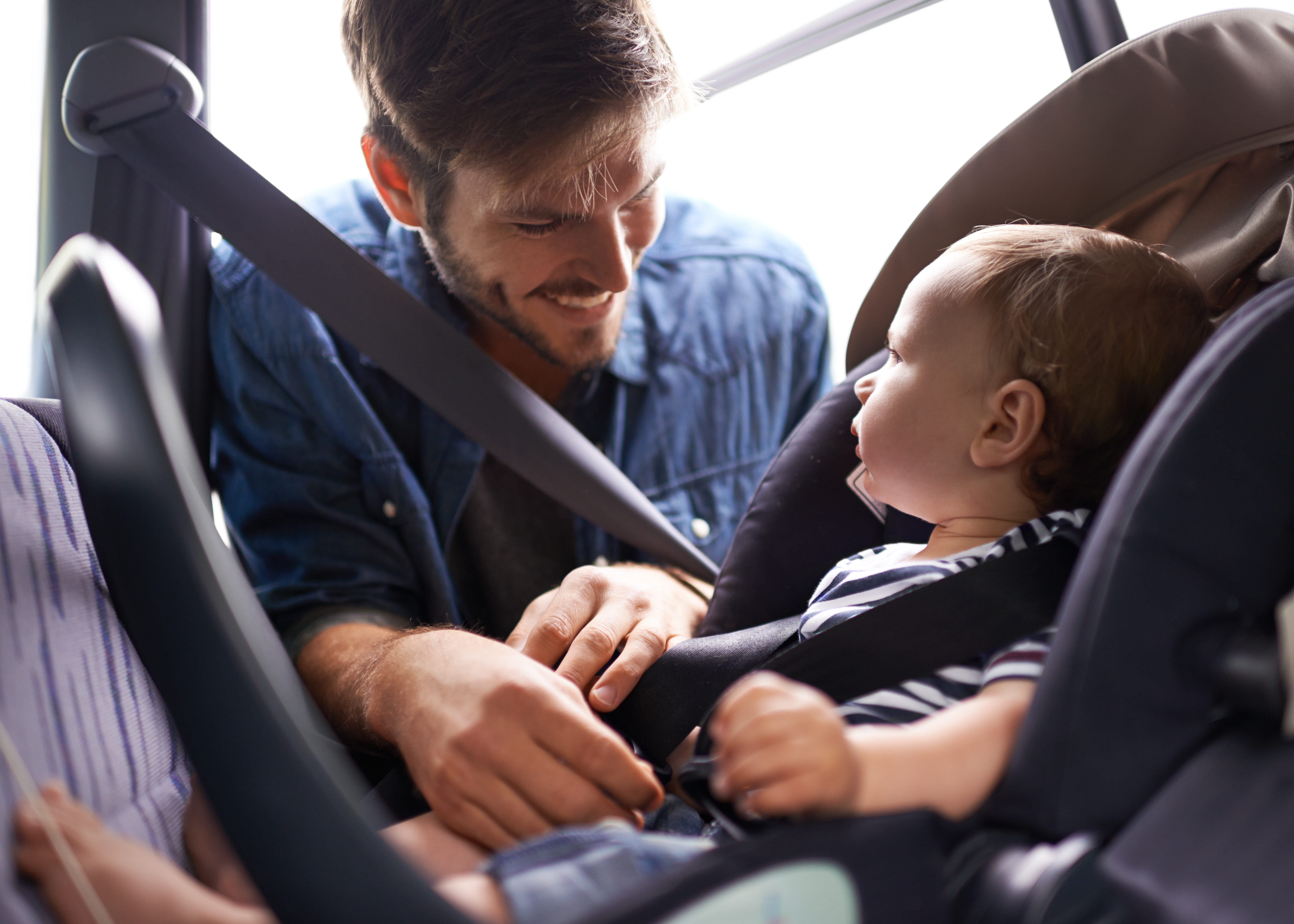 Homem sorridente ajustando o cinto de segurança de um bebê em uma cadeirinha de carro.