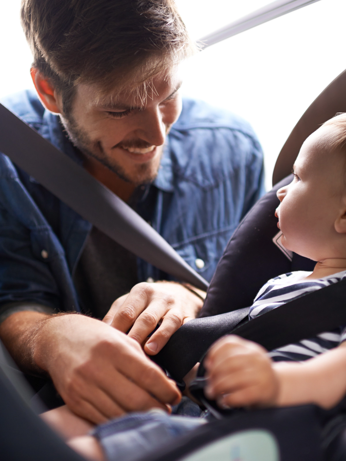 Homem sorridente ajustando o cinto de segurança de um bebê em uma cadeirinha de carro.