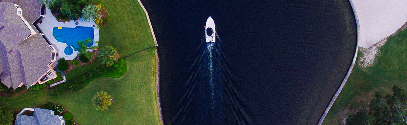 Vista aérea de um barco a navegar num canal junto a casas com piscina