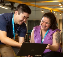 Uma mulher e um homem, em frente a um computador, trabalhando e sorrindo
