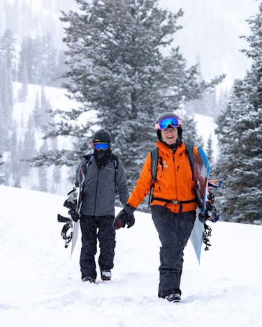 A smiling tour guide leads a snowboarder on foot across the snow