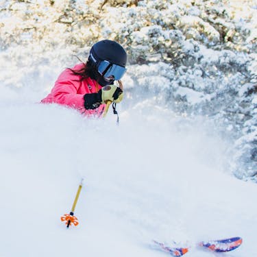 A female skier smiles as she slashes through powder