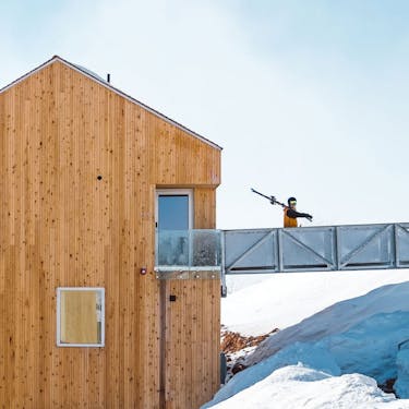 A skier carries his skis across the entry walkway of a Horizon Cabin