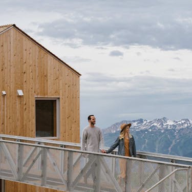 A man and a woman exit a Horizon cabin holding hands with a mountain backdrop