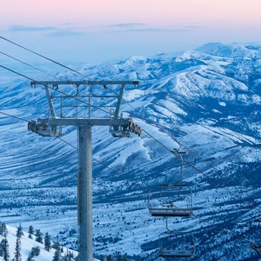 A chairlift with a snowy mountain range and pink sunset in the background