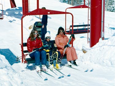 Two women and one young boy sit on a red chairlift